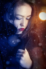 pensive girl in black coat under falling snow
