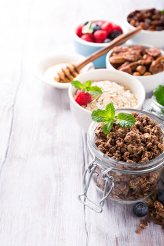 Homemade chocolate granola ingredients, nuts, oats, honey and berries on white wooden background. Healthy breakfast concept with copy space.