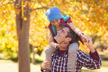 Naklejka premium Cheerful father carrying son on shoulder at park