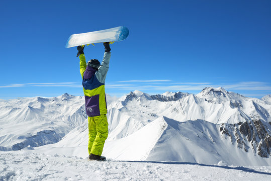 Back view of snowboarder holding board in arms raised
