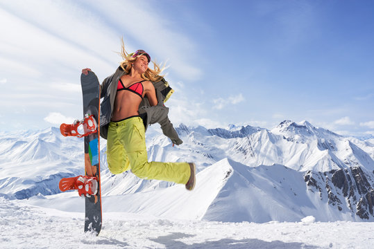 Happy young woman with snowboard jumping in winter sportswear