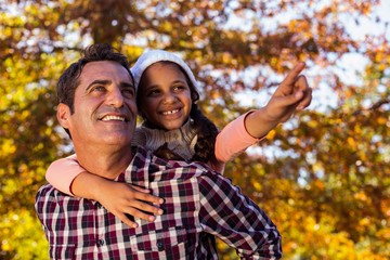 Daughter gesturing while piggybacking with father at park