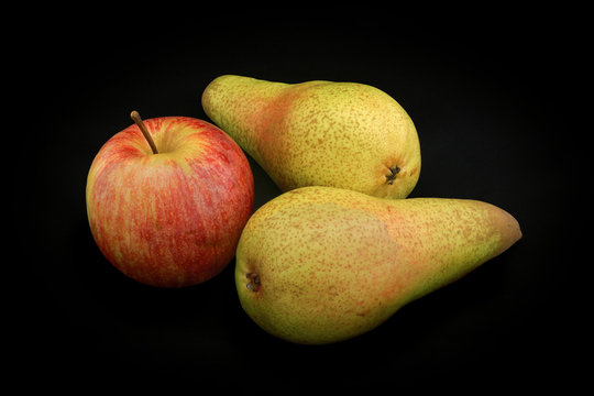 Apple of red color and two pears of yellow color on a black back