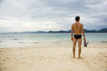 Fototapeta na wymiar Man standing on a beach and holding scuba mask. Horizontal outdoors shot
