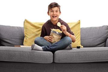 Cheerful boy sitting on a sofa and eating potato chips