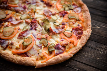 Pizza with salami, pickles, tomatoes, cheese and ham on a dark wooden background, top view