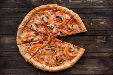 Pizza with salami, pickles, tomatoes, cheese and ham on a dark wooden background, top view