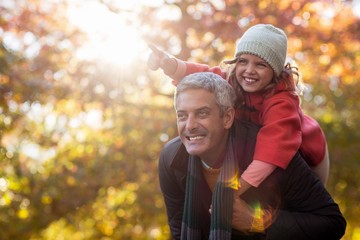 Father piggybacking daughter against autumn trees