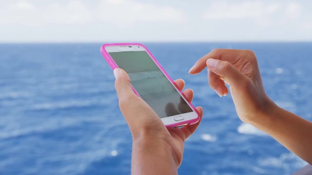 Smart phone close up - woman using smartphone app at ocean cruise at sea by the beach looking at vacation travel photos. 96 FPS SLOW MOTION.