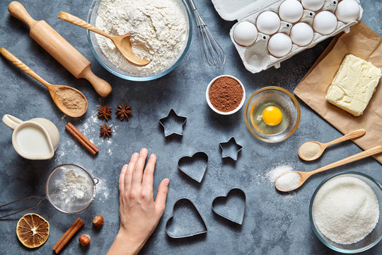 The process of making ginger cookies heart on Valentine's Day. Woman's hand ready to knead the preparing ginger cake. Baking ingredients for homemade pastry on dark background. Top view.