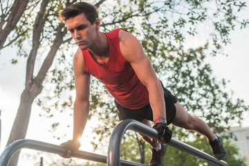 Fit young man doing push ups on horizontal bar outdoors