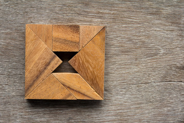 Wooden tangram as square with hourglass inside shape on old wood