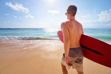 It's time for surfing! Young man holding surf board on the sea shore.