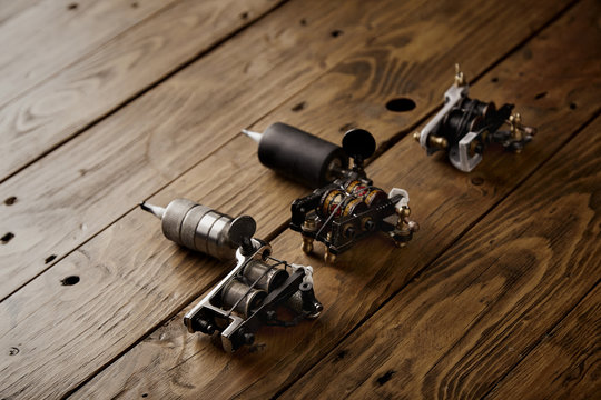 Three different custom professional tattoo guns arranged on a brown wooden table
