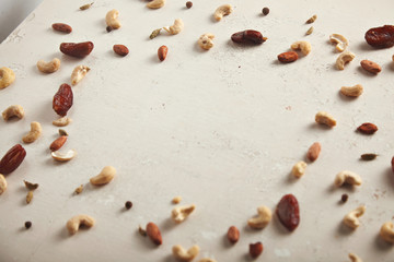 Various mixed nuts and dried fruits lying around an empty center on a white roughly painted old table