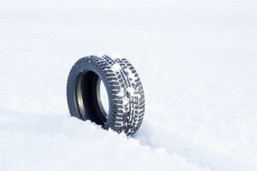 Black rubber tire rolling on the soft, fresh snow in the sunny day. White background. Seasonal tire change.