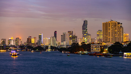 Obraz premium Boats cruising on the Chao Praya River at Bangkok, Thailand. Scenic illuminated skyline at dusk in the background.