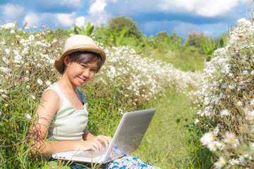 Fototapeta premium Asia teenage girl use laptop in Chrysanthemum field background sky blue.
