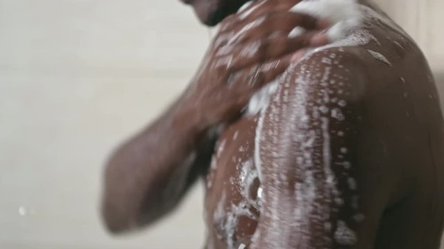 Closeup of African man cleaning his body with foamy bath buff under shower