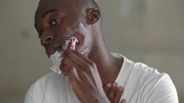 African man with foam on his face using razor to shave off beard