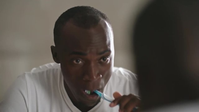 African man looking in the mirror and cleaning his teeth with toothbrush and paste