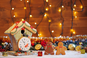 Christmas Gingerbread House with clock and two cookies man with fir festive decoration with snow on blurred bokeh background.