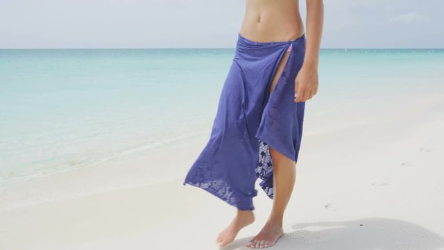Caribbean vacation travel - woman leg closeup walking on white sand relaxing in beach cover-up pareo beachwear. Sexy lean and tanned legs. Summer holidays, weight loss or epilation concept.