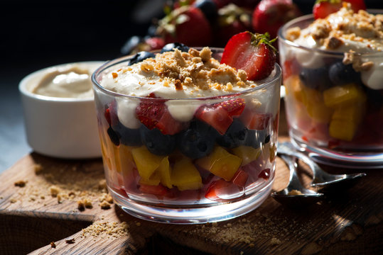 Assorted fresh fruit with custard in glasses on dark background