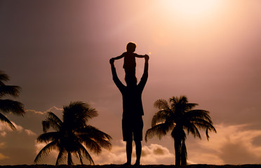 Father and little daughter silhouettes play on beach at sunset