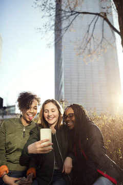 Happy multi-ethnic friends taking selfie through smart phone in city