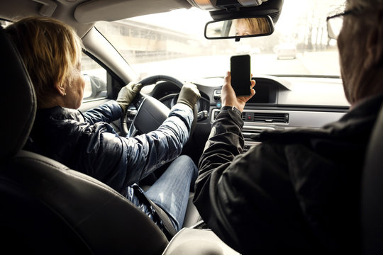 Senior woman driving car while sitting by man taking selfie through smart phone - Powered by Adobe