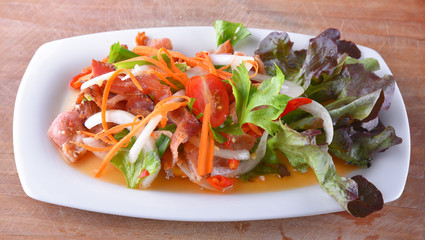 Salad with crispy bacon in dish on wooden background