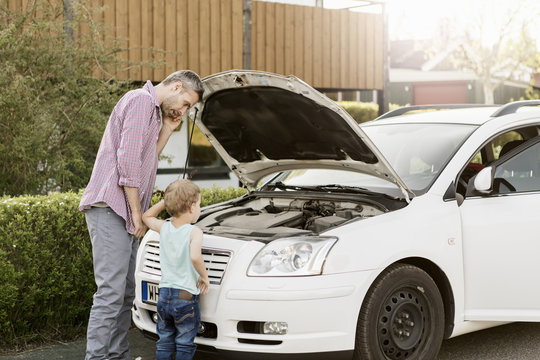Father with his son talking on phone and looking at car engine 