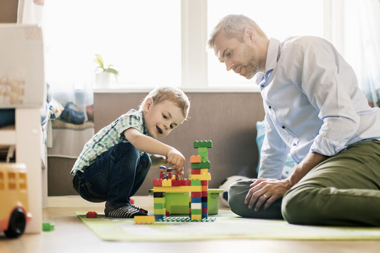 Father and son playing with toy blocks while sitting at home