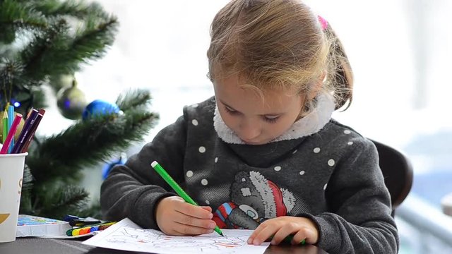 Cute happy little girl playing with crayons. Christmas background. Christmas lights background