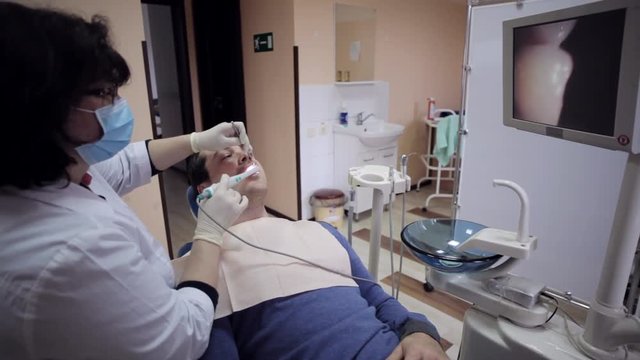 Dentist examining the mouth of a patient with an intraoral camera.