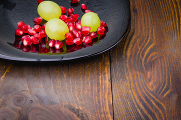 pomegranate and grapes in a plate/pomegranate and grapes in a plate on a wooden background