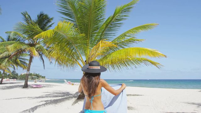 Woman on beach walking with floppy sun hat and towel for sunbathing. Girl wearing bikini relaxing on beach on Barbados, Caribbean. RED EPIC SLOW MOTION.