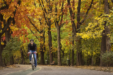 Man with his bike enjoying driving in park in autumn time, with