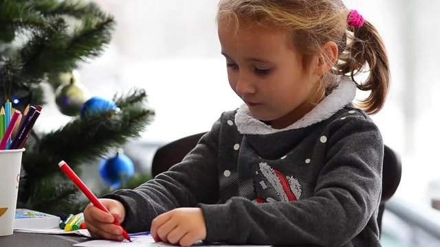 Cute happy little girl playing with crayons. Christmas background. Christmas lights background