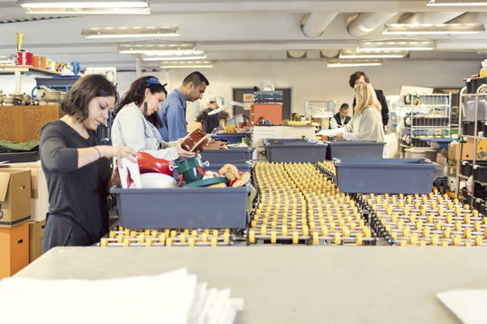 Serious volunteers checking objects in crates on production line at illuminated workshop
