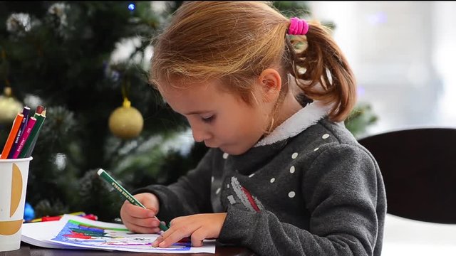 Cute happy little girl playing with crayons. Christmas background. Christmas lights background