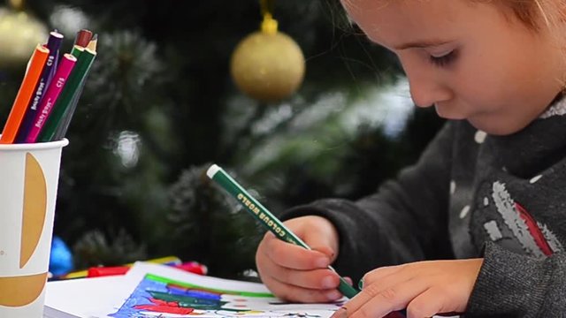 Cute happy little girl playing with crayons. Christmas background. Christmas lights background