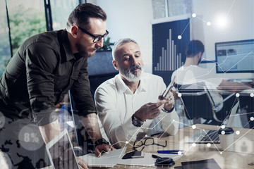 Concept of digital screen,virtual connection icon,diagram, graph interfaces.Adult bearded man using mobile tablet with young business partner.Coworking people meeting process.Blurred background.