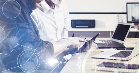 Concept of digital screen,virtual connection icon,diagram,graph interfaces.Bearded young man holding mobile phone and touching display.Adult businessman working together with partner.Film effect,wide