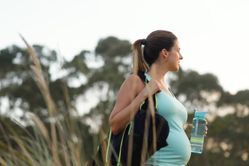 Fitness pregnant woman drinking water after outdoor workout. Healthy and active pregnancy lifestyle concept.