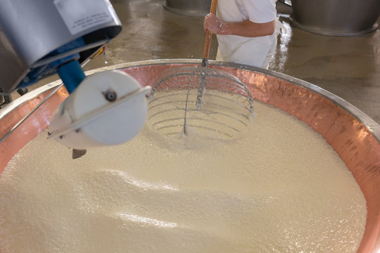 Worker stirring curd in copper tub of cheese factory making parmesan 