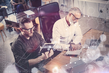 Concept of digital screen,virtual connection icon,diagram, graph interfaces.Bearded young man working together with adult businessman at the wooden table.Coworkers teamwork in modern office.Flare.