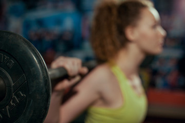 Young girl doing back squat in gym with barbell.