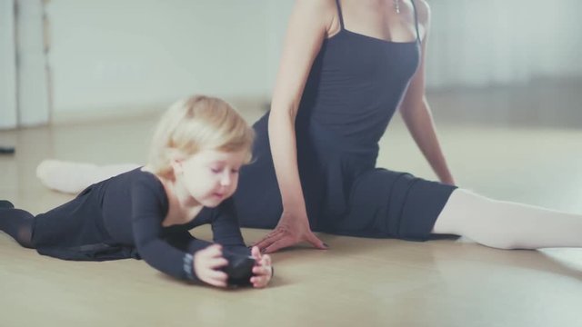 Little Ballerina diligently doing stretching in ballet class sitting on the floor. An adult woman and a little girl ballerina train together. Dance teacher and a little schoolgirl sitting on the floor